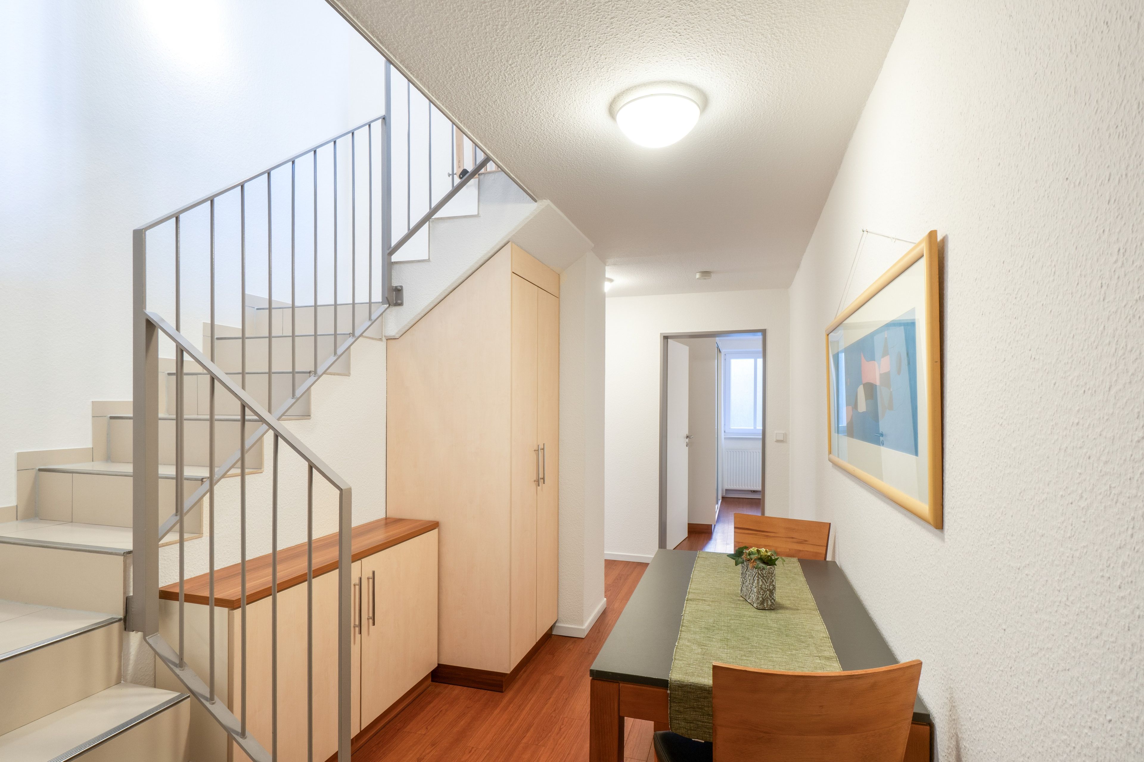 A modern interior with a staircase, a dining area, and a hallway leading to another room.