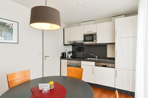 A modern kitchen with white cabinets, a microwave, and a stove. There's a dining table with chairs and a pendant light above it. - 5-Star Comfort Holiday Home Jümmers: 'Hein Mück', Prime Location by the Wadden Sea National Park (Wangerland-Horumersiel)