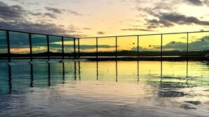Un área tranquila de piscina al aire libre con suelo de baldosas y barandilla que da a un cuerpo de agua, reflejando el cielo.