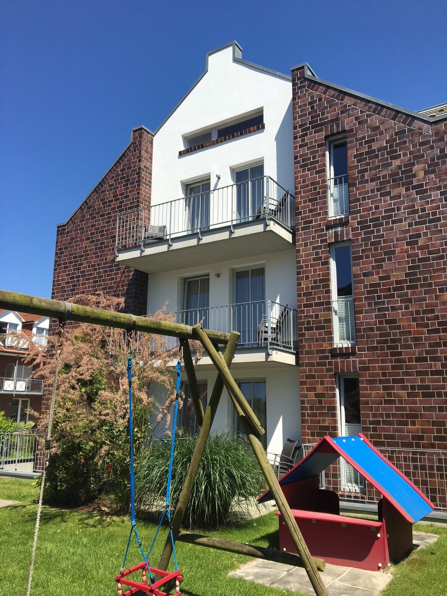 Ein zweigeschossiges Gebäude mit Ziegelverkleidung, einem Balkon im oberen Stockwerk und einer Schaukel im Vordergrund.