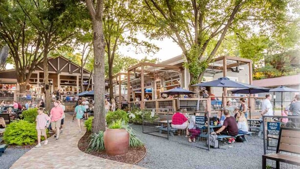 An outdoor dining area with tables and umbrellas, surrounded by trees and a brick pathway. - Near McKinney Square!  Charming 3 BR house with garage and huge yard (McKinney)
