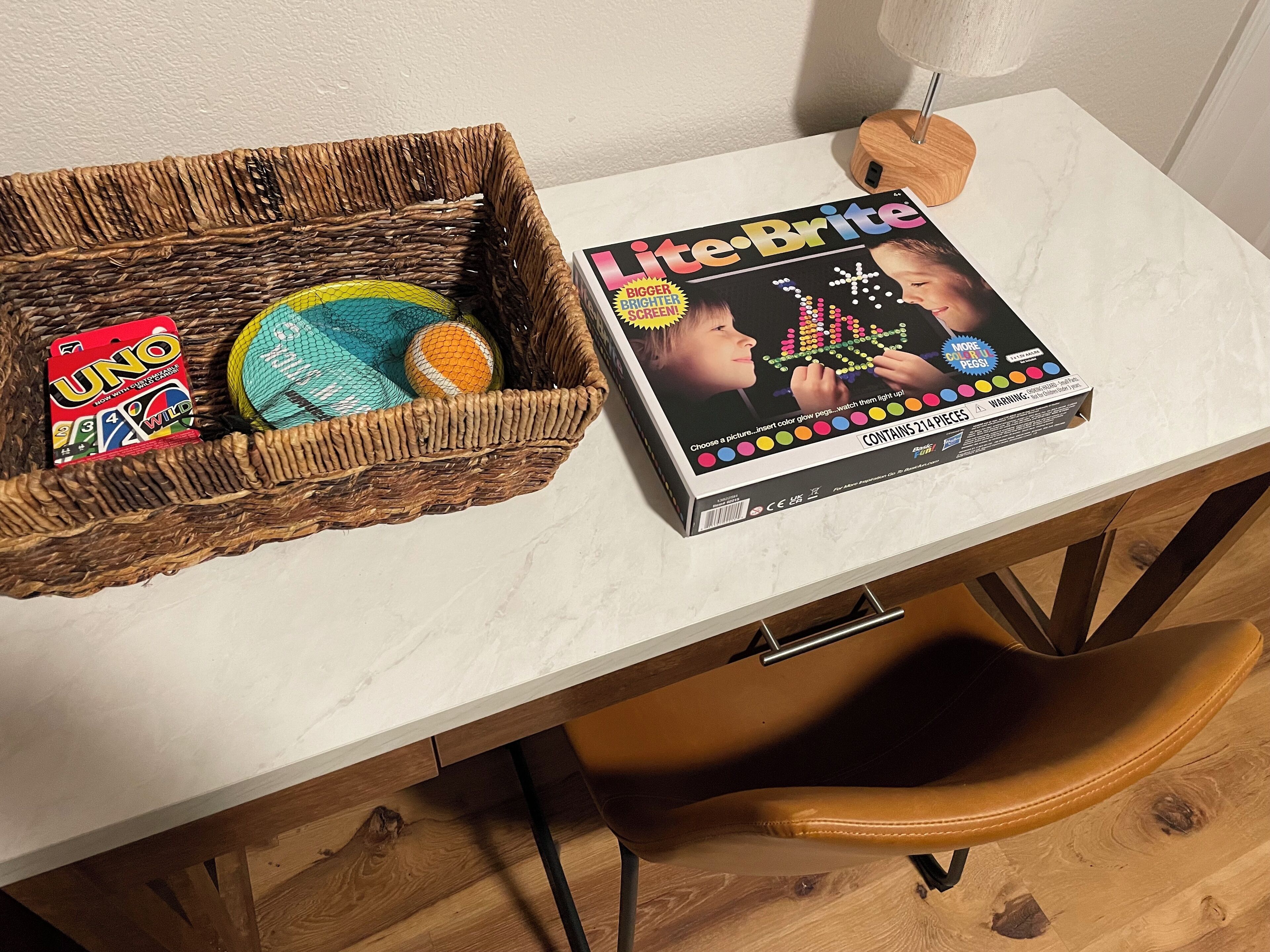 Ett bord med en flätad korg som innehåller UNO-kort och en Lite-Brite-leksak, och en tidning med titeln ”Lite-Brite” ligger på en bänkskiva i marmor.