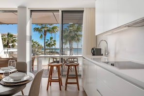 A modern kitchen with a built-in sink, wooden stools, and a dining area with a table and chairs. - Casa Costa Tropical (Estepona)