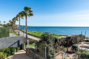 A coastal walkway with palm trees, a stone wall, and a view of the sea. - Casa Costa Tropical (Estepona)