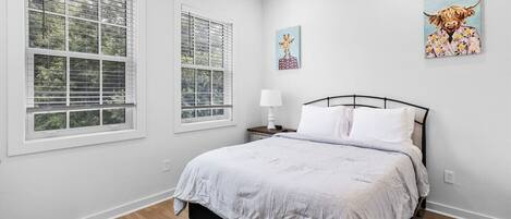 Une chambre à coucher comprenant un lit, deux fenêtres, une table de chevet et deux œuvres d’art murales.