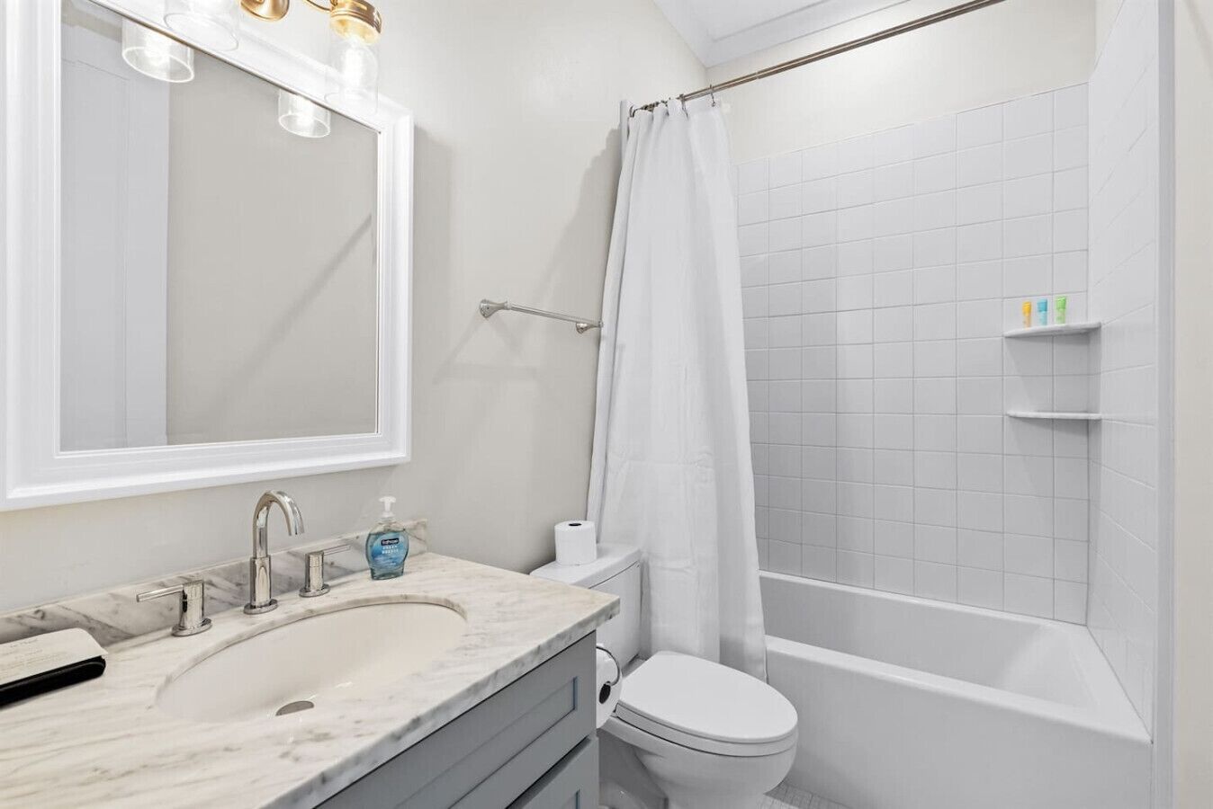 Un baño con lavamanos blanco, espejo y retrete, cortina de ducha y zona de ducha con azulejos.