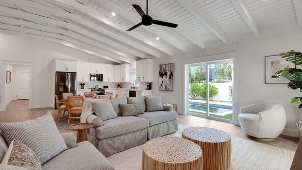 A spacious living area with a modern kitchen, a ceiling fan, and a large window providing a view of the outdoors. - Honey I'm Holmes - New Home Near the Beach! Turf (Holmes Beach)