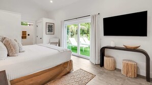 A bedroom with a bed, a TV mounted on the wall, a sliding glass door leading to a balcony, and a small table with stools. - Honey I'm Holmes - New Home Near the Beach! Turf (Holmes Beach)