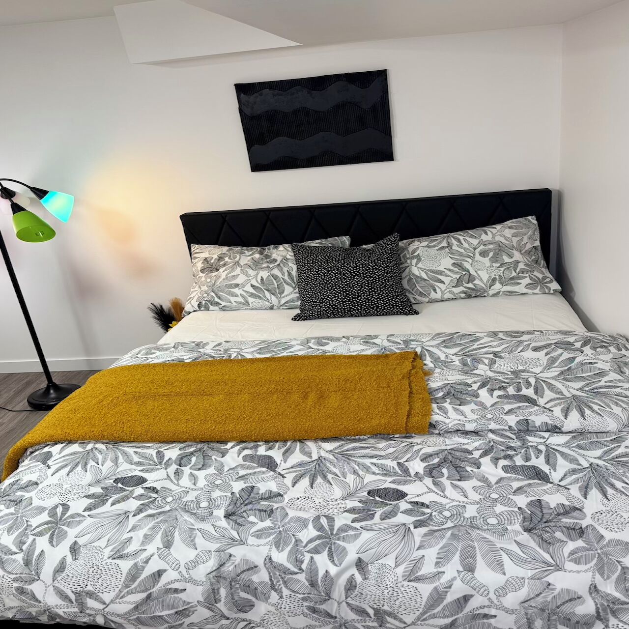 Cama bem arrumada com roupa de cama florida, cabeceira preta e manta amarela mostarda.