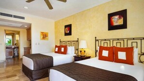 A hotel room with two beds, a small table with a lamp, and artwork on the walls. - Villa Del Arco (Cabo San Lucas)