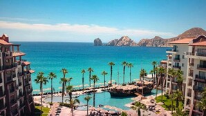 A resort with a pool area, palm trees, and a view of the ocean. - Villa Del Arco (Cabo San Lucas)