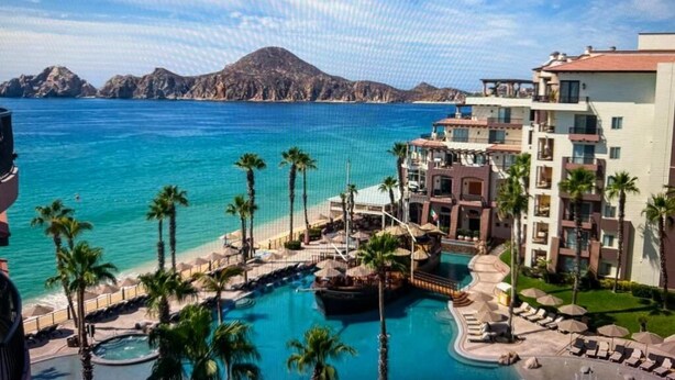 A resort with a pool, palm trees, and a view of the ocean. - Villa Del Arco (Cabo San Lucas)