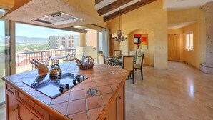 A spacious kitchen with a large island, a dining area with chairs, and a view of the cityscape. - Villa Del Arco (Cabo San Lucas)