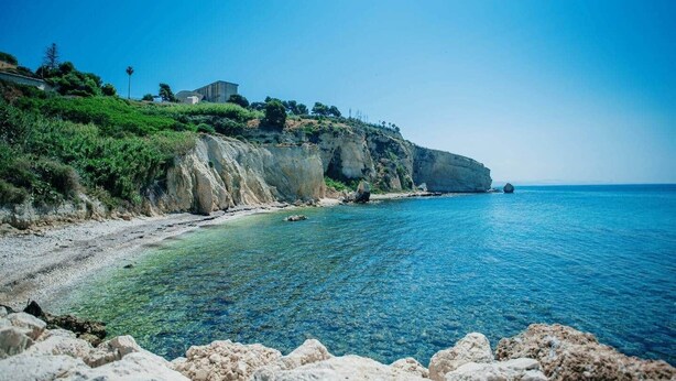 A coastal landscape with a clear blue sea, rocky cliffs, and a building on the cliff. - La Luna sul Porto by Biddizzi Rari - at the port, near the sea and the center (Sciacca)