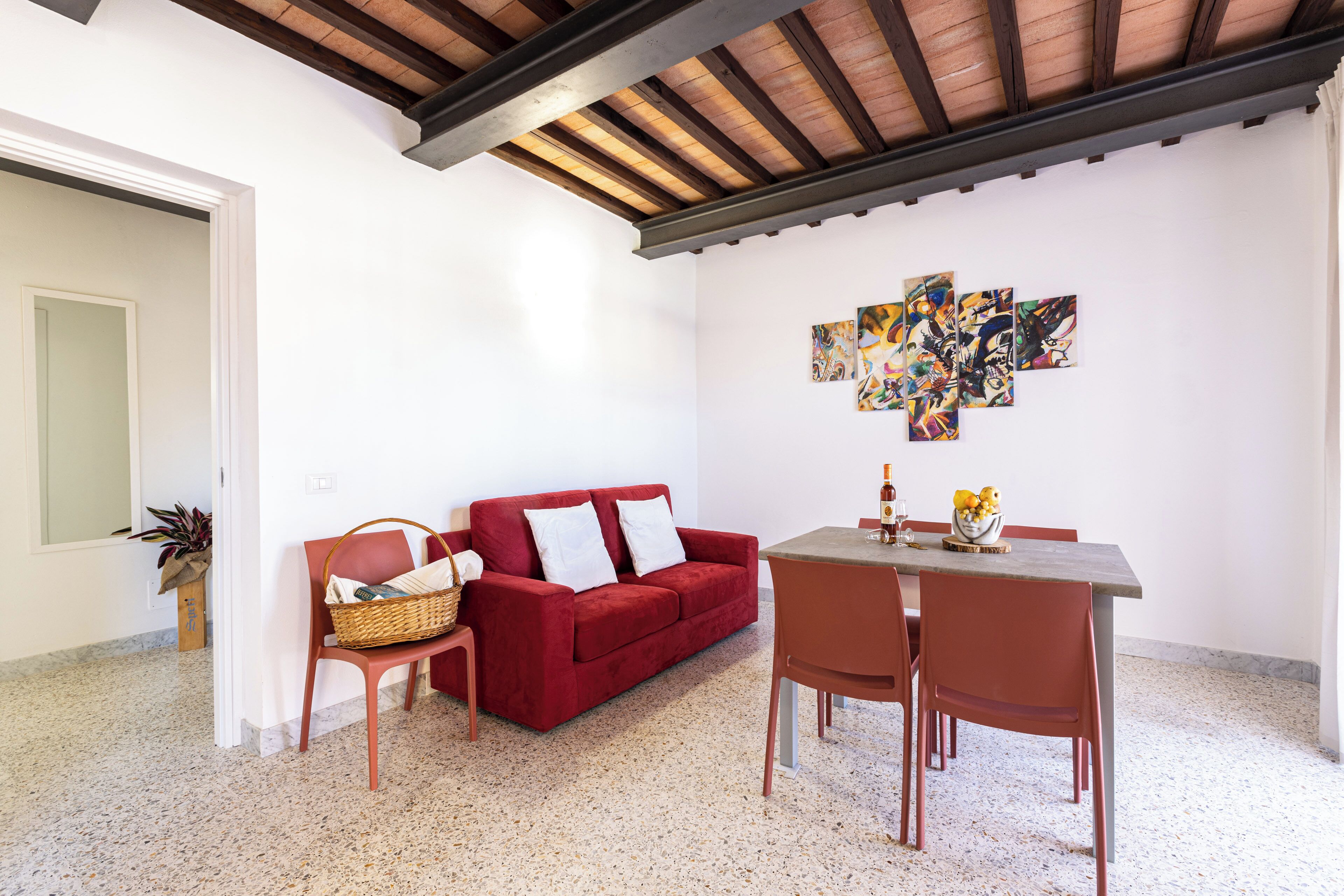 A living area with a red sofa, a wooden dining table, and a modern abstract art piece on the wall.