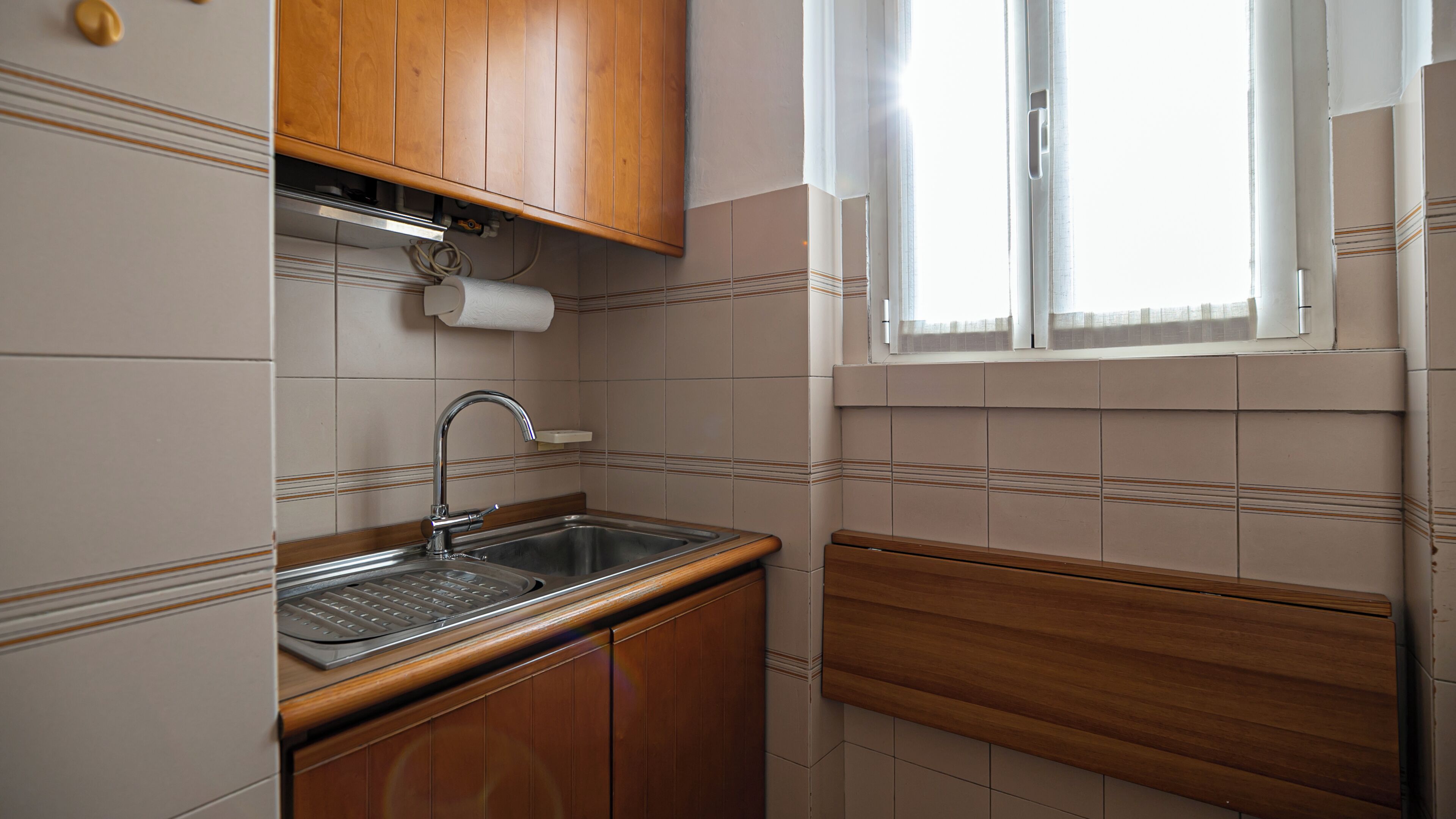 A small kitchen with wooden cabinets, a stainless steel sink, and a window with a view.