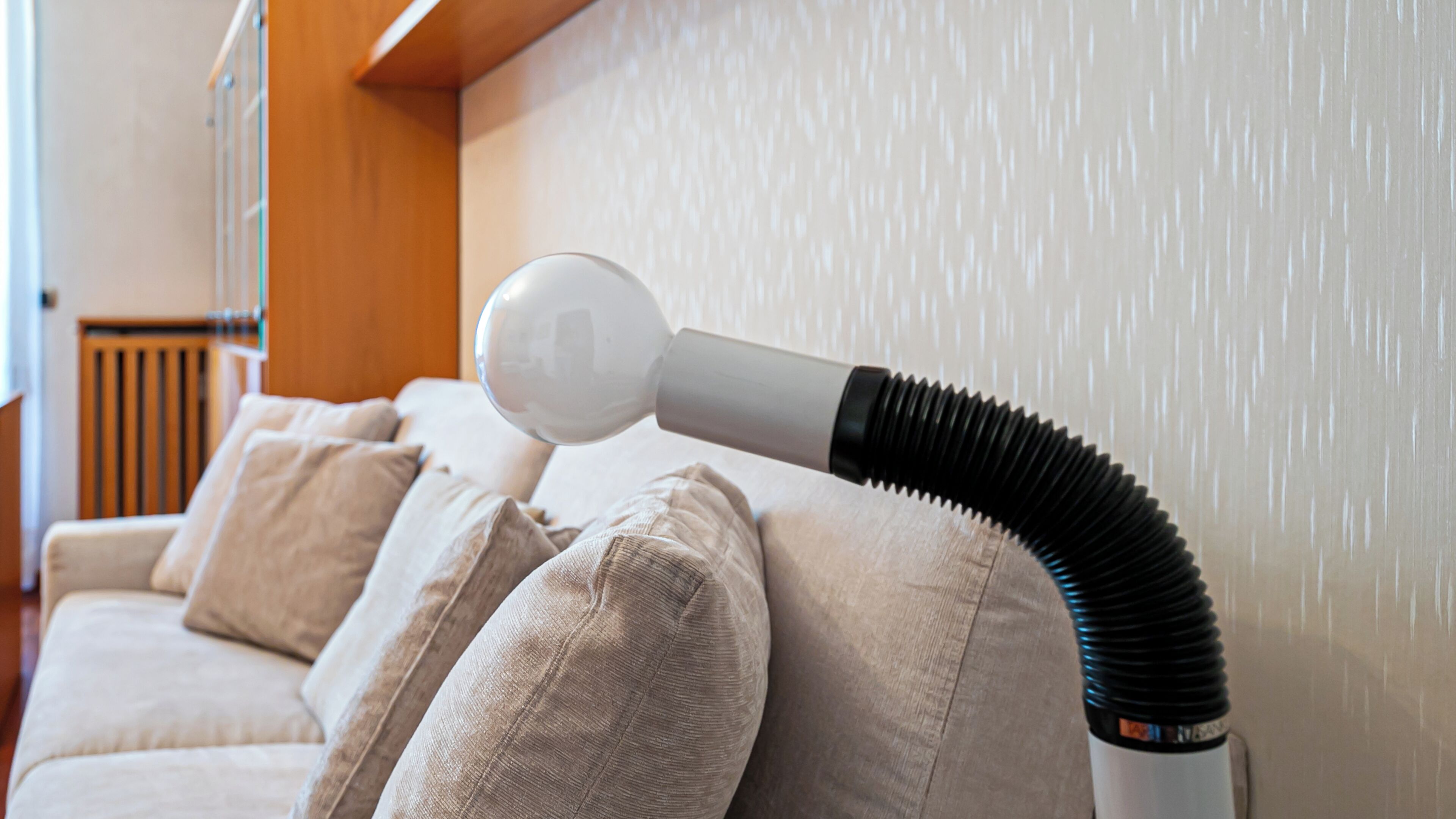 A room with a beige sofa and a white vacuum cleaner with a black hose.