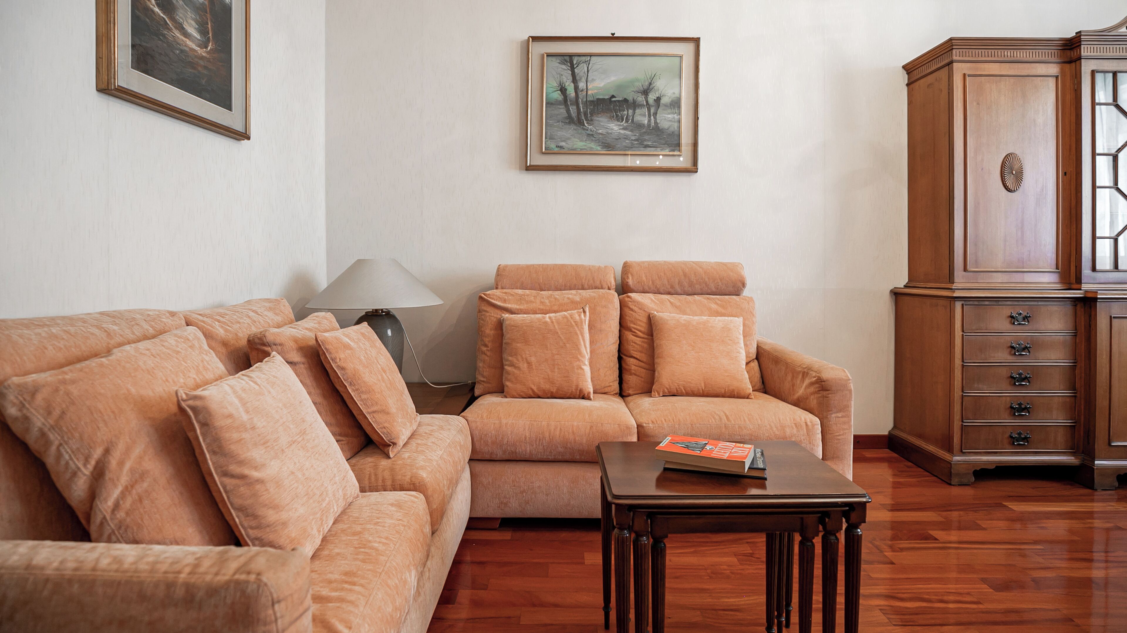 A living room with a sectional sofa, a small table, a lamp, and a cabinet.