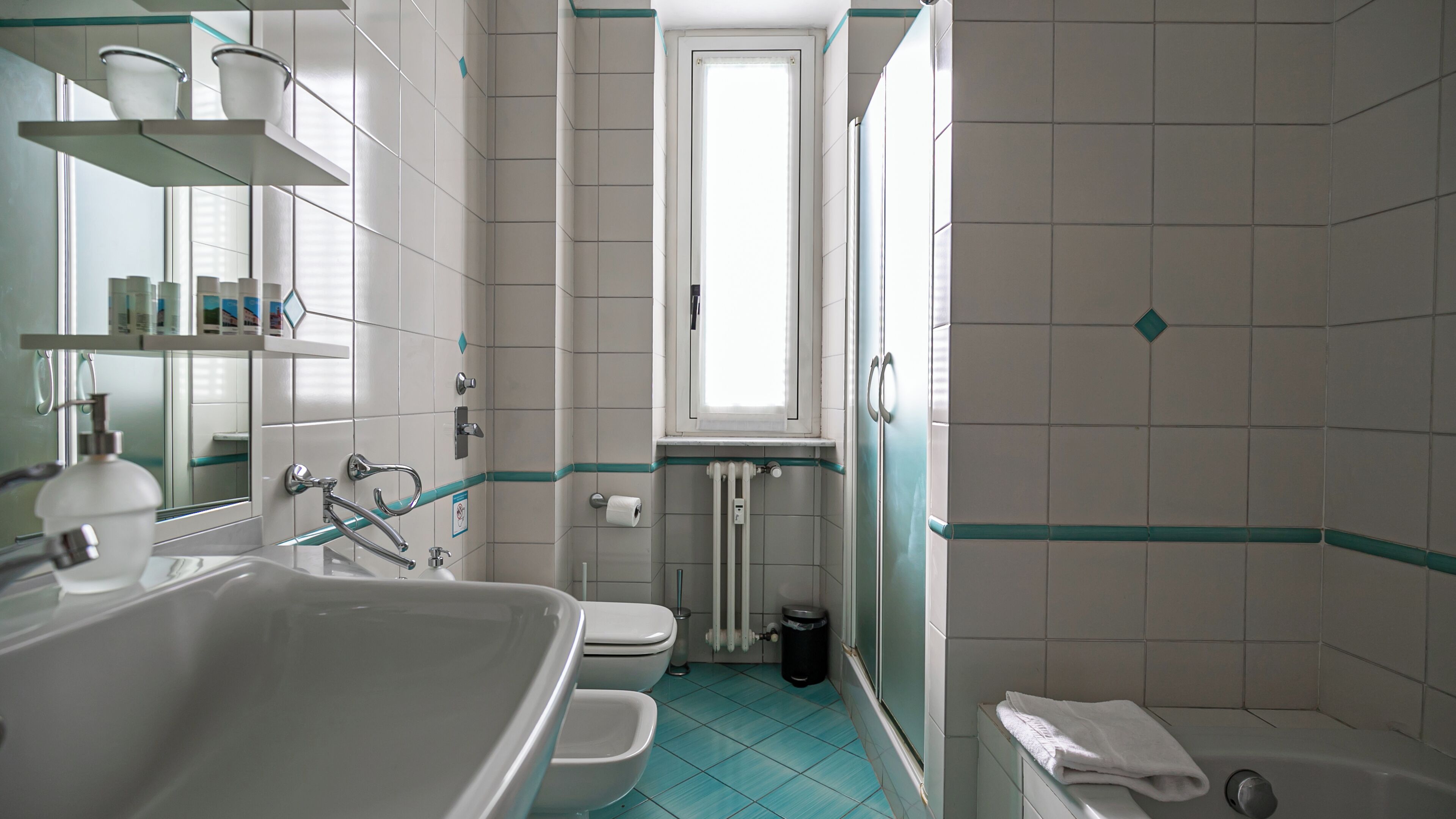 Une salle de bain avec un lavabo, des toilettes et une baignoire. Il y a une fenêtre au-dessus des toilettes et les murs sont recouverts de carreaux.