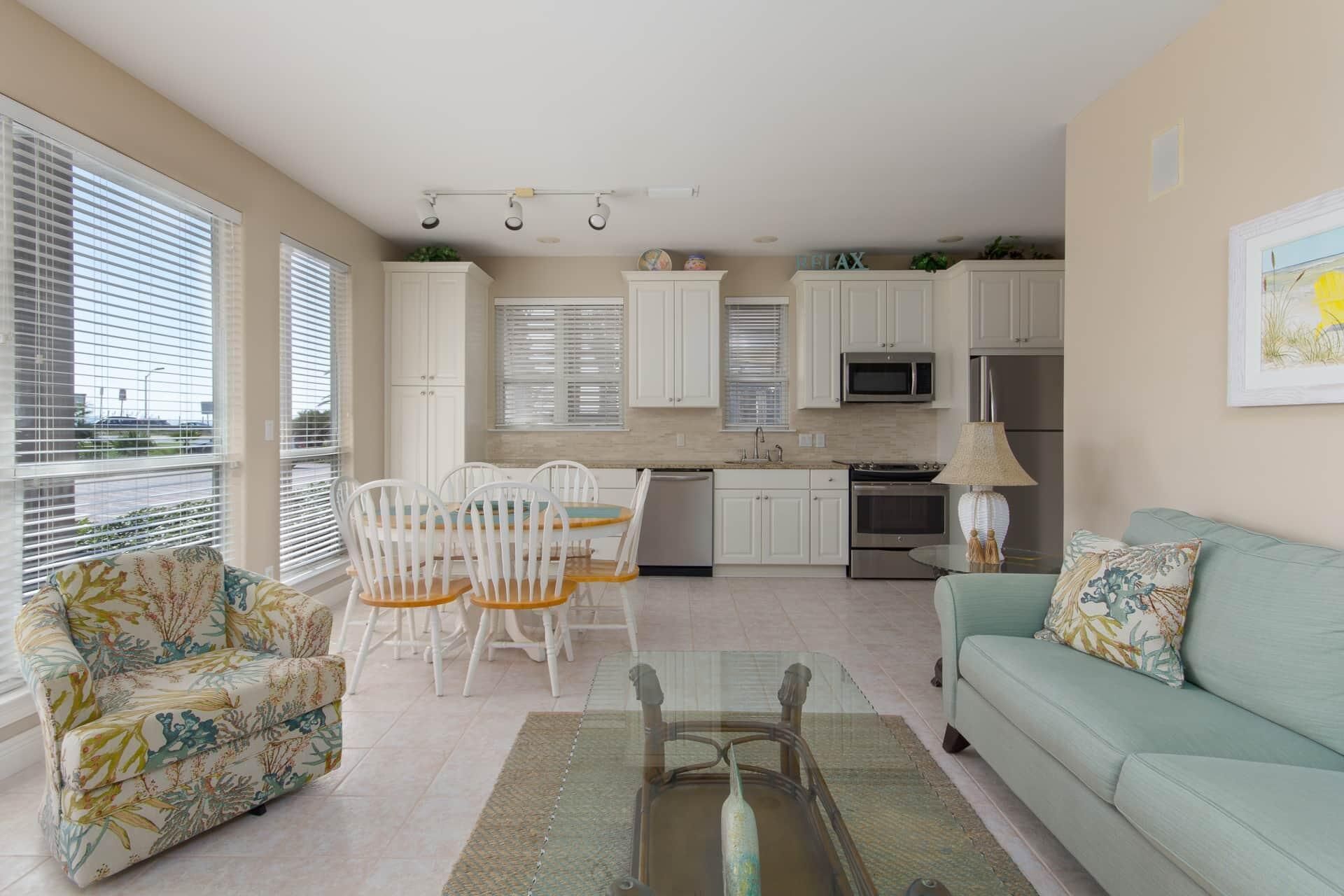 A modern kitchen with white cabinets, a dining area with a glass table, and a living room with a green sofa.
