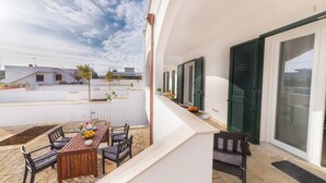Uma varanda com mesa e cadeiras de madeira, uma pequena área de jardim e vista para o bairro.