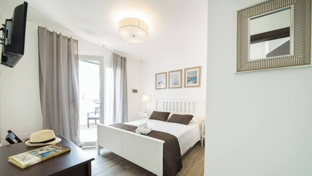 Quarto de hotel com cama, mesa de cabeceira, luminária e vista para o exterior.