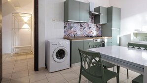 Cozinha compacta com máquina de lavar, mesa de jantar e cadeiras verdes.