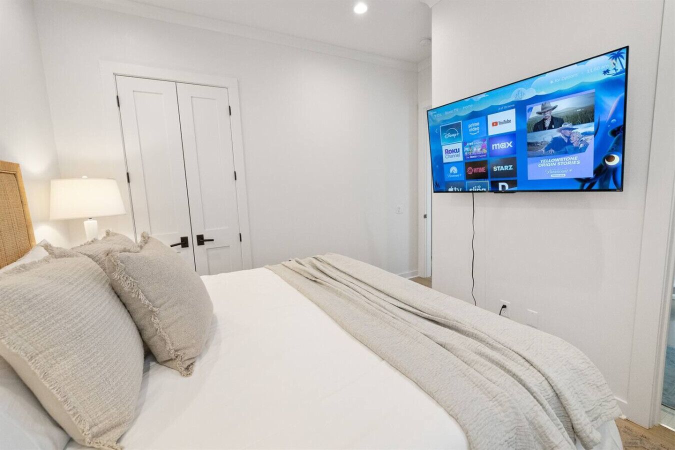 A hotel room with a large bed, a TV mounted on the wall displaying various streaming services, and a door with a light switch.