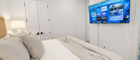 A hotel room with a large bed, a TV mounted on the wall displaying various streaming services, and a door with a light switch.