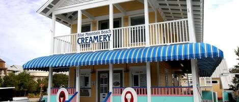 A creamery with a blue and white striped awning, a signboard, and a small outdoor seating area.