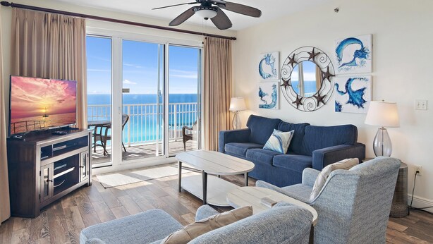 A living room with a sofa, chairs, a coffee table, a TV, and a balcony with a view of the ocean. - Ariel Dunes I 2301 (Miramar Beach)