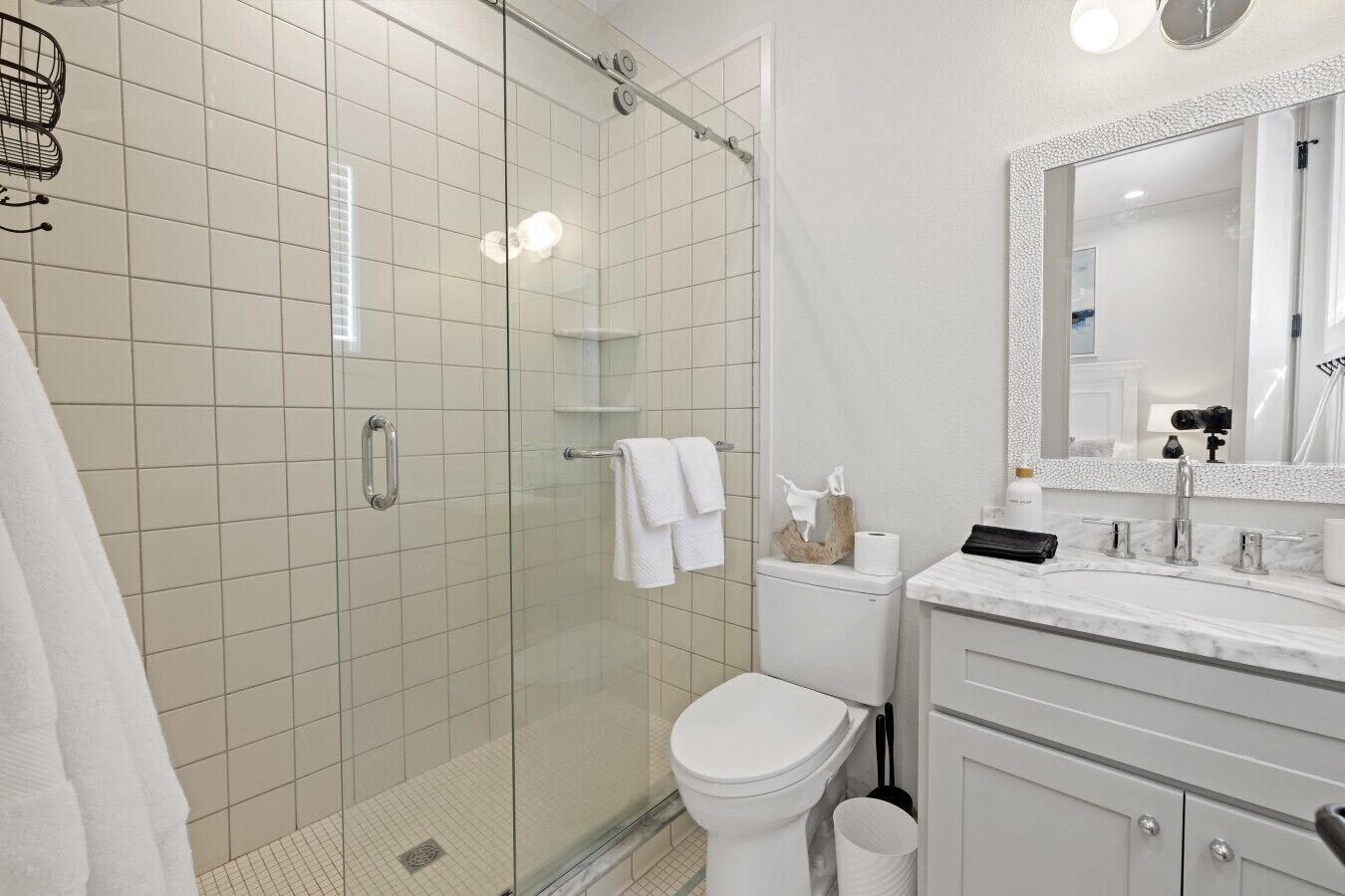 Een moderne badkamer met een glazen douchecabine, een wit toilet, een marmeren wastafel en een grote spiegel.