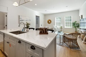 A modern kitchen with a large island, white cabinetry, and a dining area with wicker furniture.
