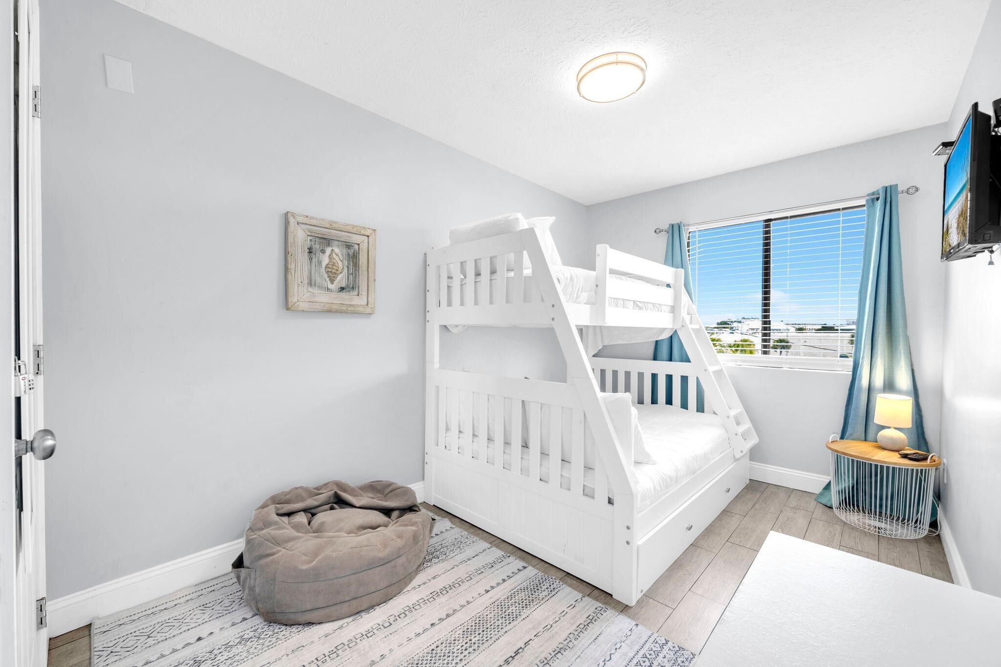 A child’s bedroom with a bunk bed, a bean bag chair, a framed picture, and a window with curtains.