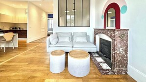A modern living room with a sofa, two round side tables, a fireplace, and a kitchen in the background. - Le Bastille / 6 pers / 300 m station / Air-conditioned (Grenoble)