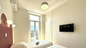 A hotel room with two beds, a TV, and a window with a view of buildings. - Le Bastille / 6 pers / 300 m station / Air-conditioned (Grenoble)
