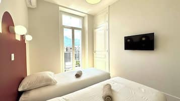 A hotel room with two beds, a TV, and a window with a view of buildings.
