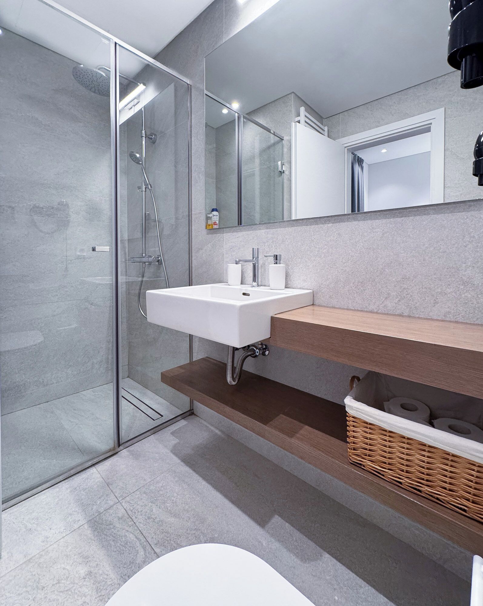 A modern bathroom with a glass shower enclosure, a white sink, and a wooden vanity.