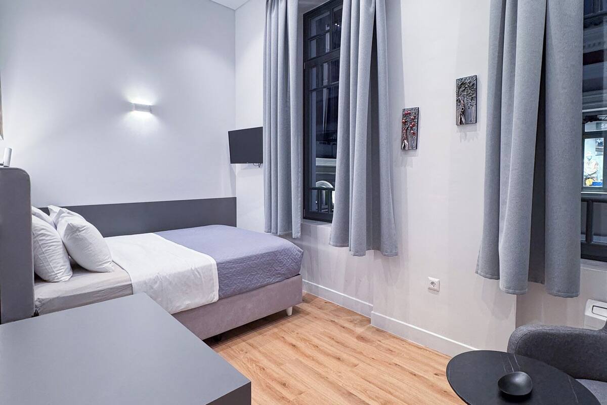 A modern hotel room with a bed, a desk, a chair, and a window with curtains.