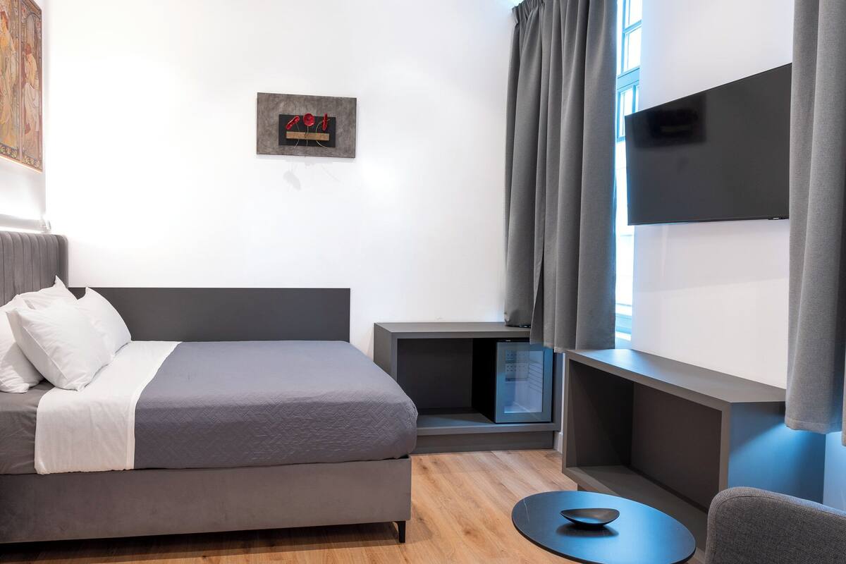 A modern hotel room with a bed, a desk, a TV, and a small table.