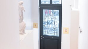A black door with a decorative glass panel, a white statue, and a wooden staircase. - Lofus Art Suites (Athens)