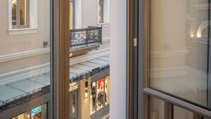 A view from a window of a building with a balcony, a storefront with a neon sign, and a clear sky. - Lofus Art Suites (Athens)