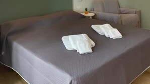 Habitación de hotel con una cama grande, una silla, una mesita con una planta y un cuadro en la pared.
