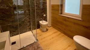 Un baño con cabina de ducha de vidrio, un bidé y una ventana.