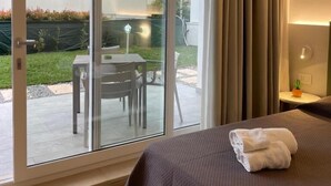 Habitación de hotel con una cama, una mesita y una silla frente a la puerta corrediza de vidrio.