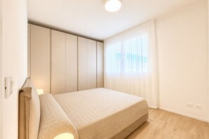 Ein Schlafzimmer mit einem Bett, einem Nachttisch, einem Fenster mit Vorhängen und einer Deckenleuchte.