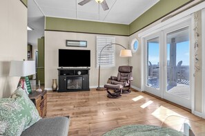 A living room with a flat-screen TV, leather recliner, and a large window with a view. - The Dolphin Pod: Oceanfront, Dog-Friendly Cottage (Oak Island)