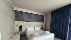 A modern hotel room with a large bed, bedside tables, a headboard with a leaf pattern, and a dark blue curtain.