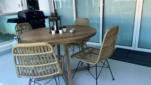 Een ronde houten tafel met vier rieten stoelen, een kleine potplant en een metalen bak.
