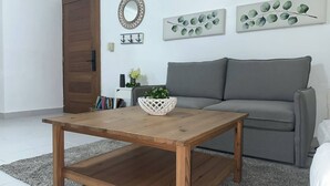 Een woonkamer met een houten salontafel, een grijze bank en decoratieve wandkunst.